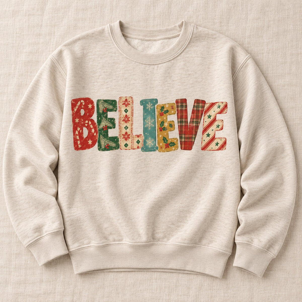 Oatmeal crewneck sweatshirt laid flat with BELIEVE spelled in vintage holiday patterns of candy canes, plaid, snowflakes and holly