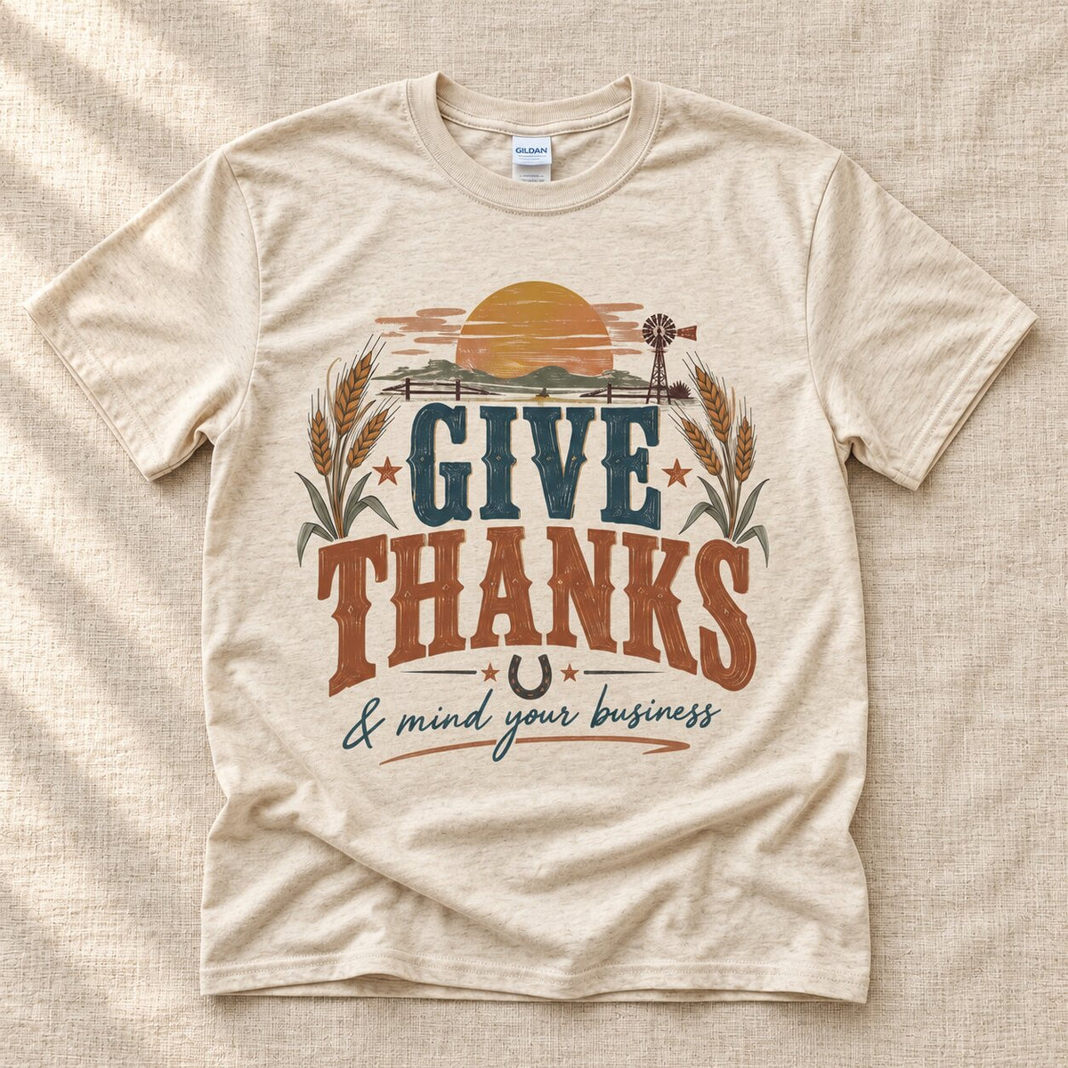 Natural Give Thanks and mind your business graphic tee laid flat, with a sunset, windmill and wheat design in navy and rust