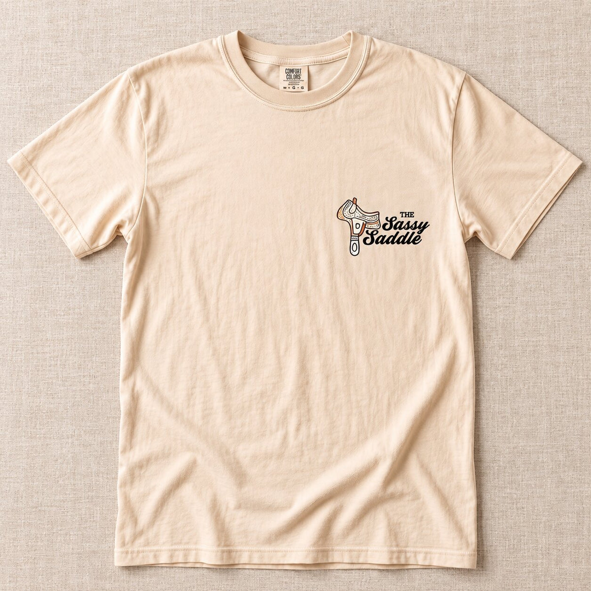 Front of the cream tee with a small Sassy Saddle logo on the left chest