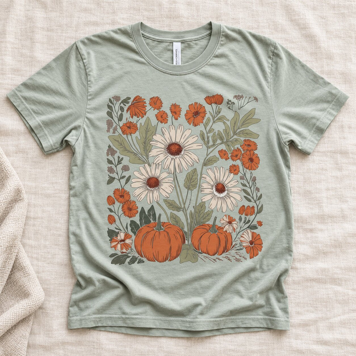 Sage green tee laid flat with orange pumpkins, white daisies and orange wildflowers in a botanical fall graphic
