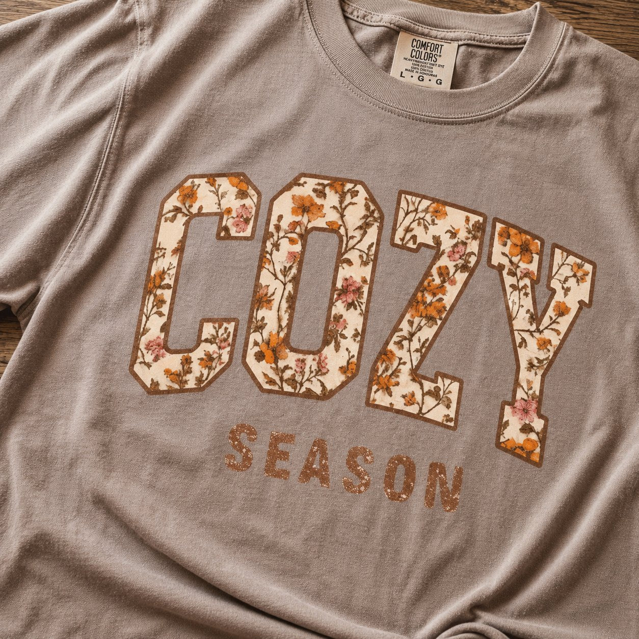 Close-up of the "COZY SEASON" graphic showing the floral-filled varsity lettering on taupe cotton fabric.