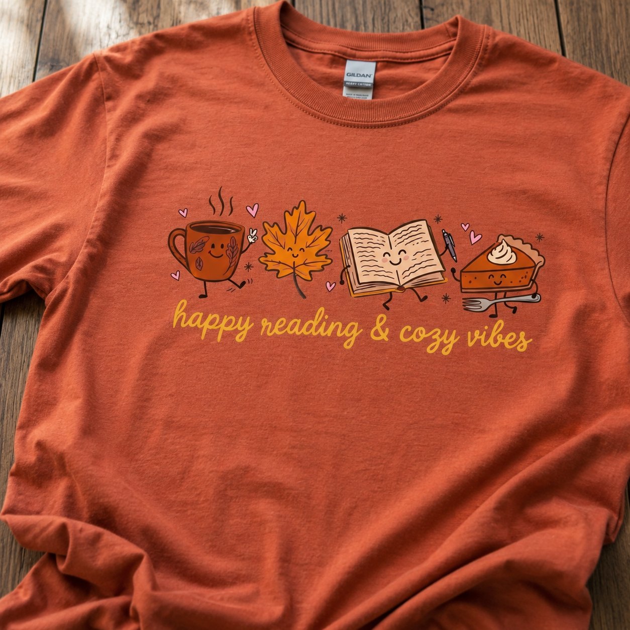 Close-up of the coffee mug, maple leaf, book, and pumpkin pie characters with the "happy reading & cozy vibes" text on burnt orange cotton fabric.