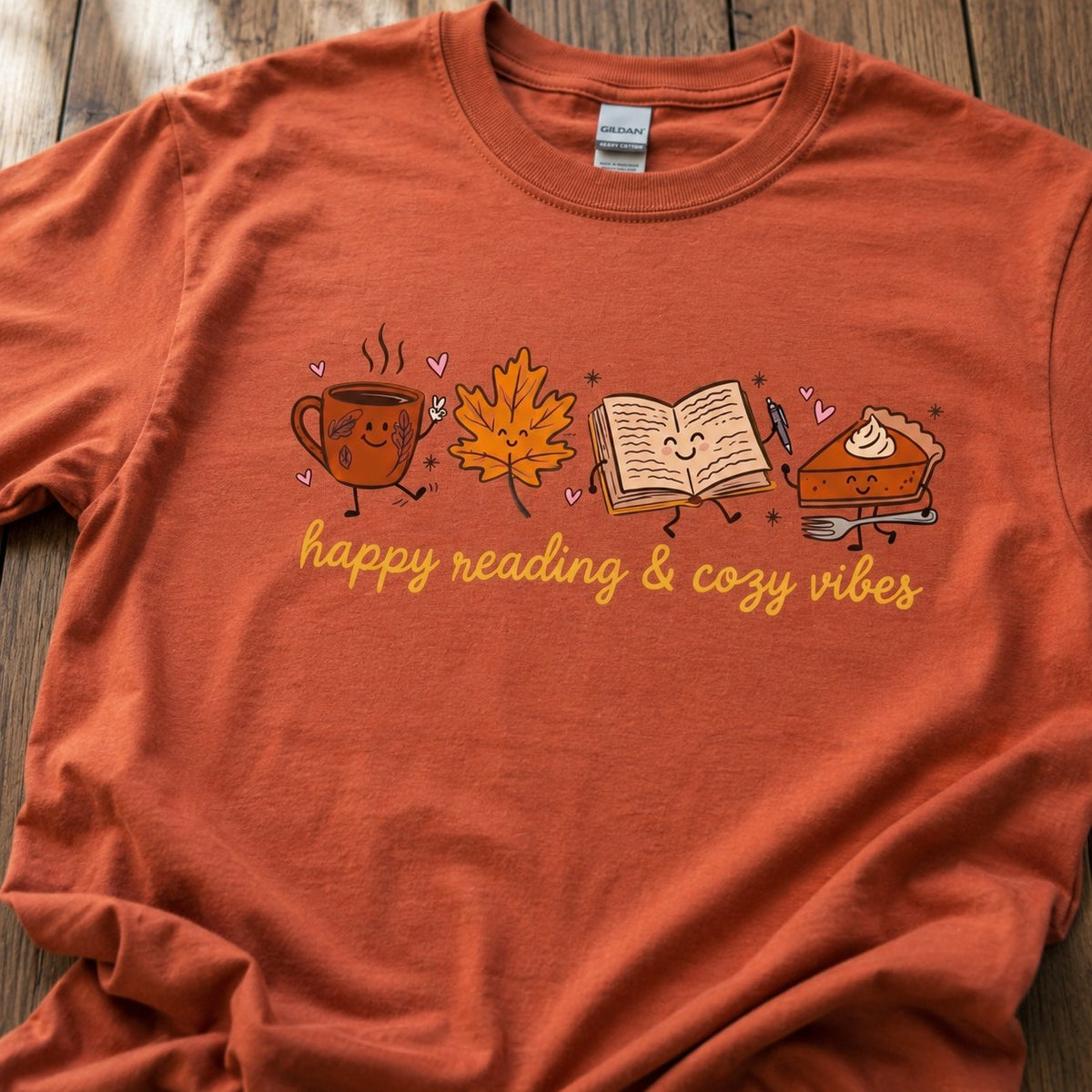 Close-up of the coffee mug, maple leaf, book, and pumpkin pie characters with the "happy reading & cozy vibes" text on burnt orange cotton fabric.
