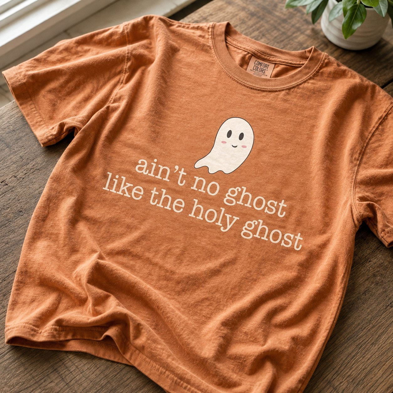 Close-up of the smiling cartoon ghost graphic and "ain't no ghost like the holy ghost" text on rust orange cotton fabric.