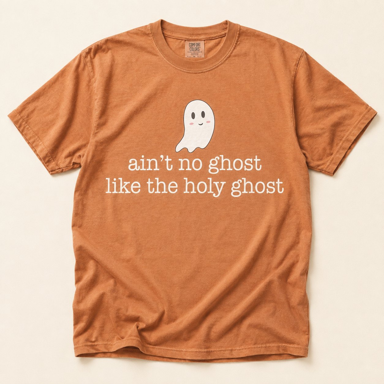 Rust orange t-shirt flat lay on a cream background printed with a small smiling cartoon ghost above the text "ain't no ghost like the holy ghost."