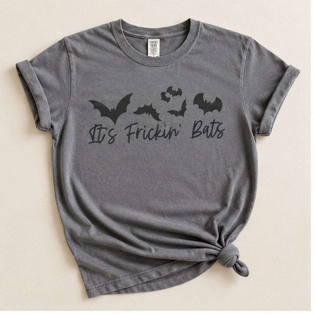 Charcoal grey t-shirt knotted at the hem, flat lay on a cream background, printed with a cluster of black bats above the script text "It's Frickin' Bats."