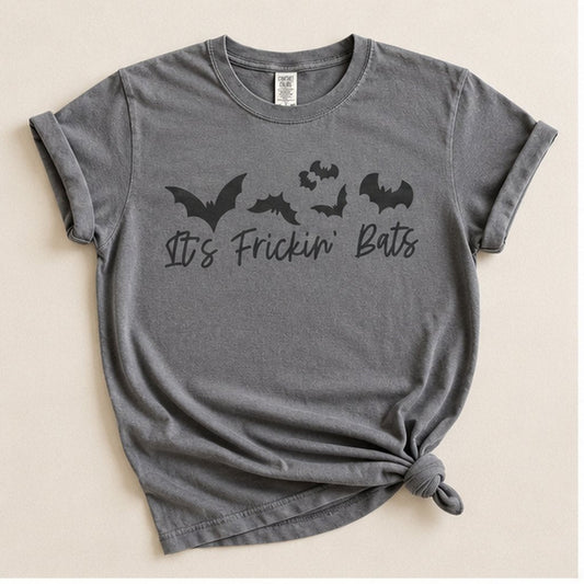Charcoal grey t-shirt knotted at the hem, flat lay on a cream background, printed with a cluster of black bats above the script text "It's Frickin' Bats."