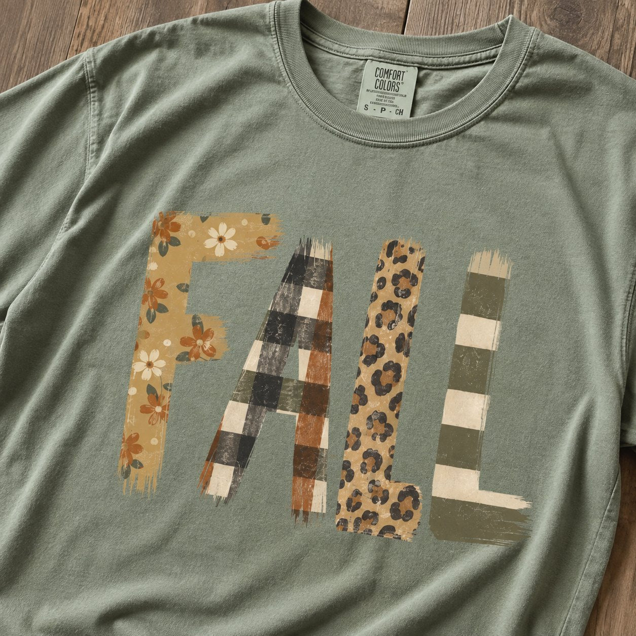 Close-up of the patchwork "FALL" graphic showing the distressed floral, buffalo check, leopard, and striped letter textures on sage green cotton.