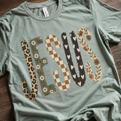 Close-up of the patchwork "JESUS" graphic showing the leopard, daisy, checkerboard, heart, and floral letter textures on sage green cotton.