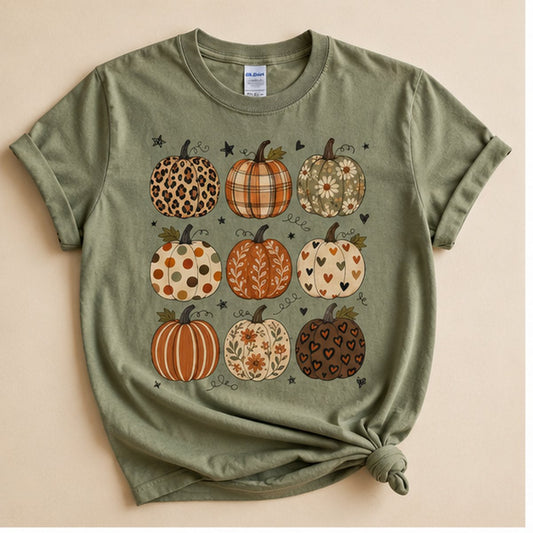 Sage green t-shirt knotted at the hem, flat lay on a cream background, printed with a 3x3 grid of nine differently patterned pumpkins (leopard, plaid, daisy, polka dot, floral, striped, and heart print).