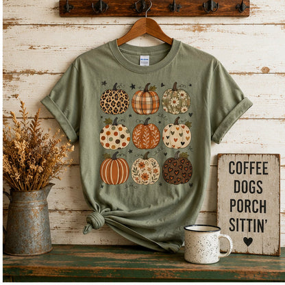 Sage green patchwork pumpkins t-shirt hanging on a rustic coat hook next to a "Coffee Dogs Porch Sittin'" sign, dried florals, and a speckled mug on a farmhouse porch.
