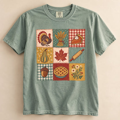 Sage green Thanksgiving patchwork graphic tee laid flat, with a quilt-style grid of turkey, wheat, pie, maple leaf, rolling pin, acorn and wildflower squares