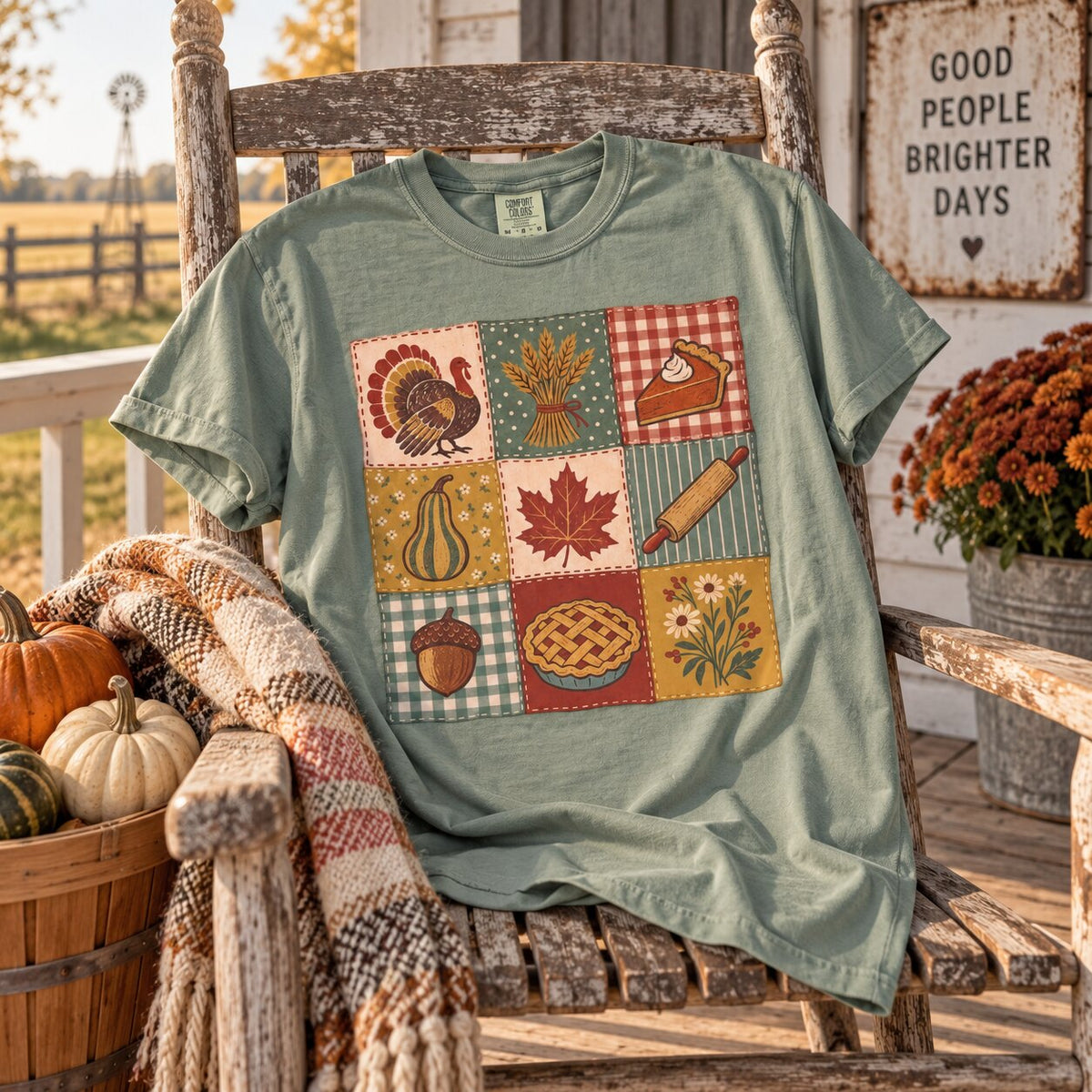 Sage green Thanksgiving patchwork tee draped over a rustic porch rocking chair with a plaid blanket, mums, pumpkins and a Good People Brighter Days sign